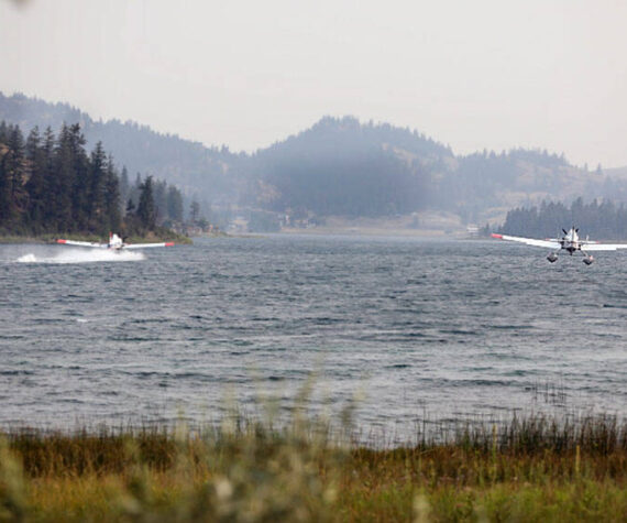 Two water-bomber planes gather water from Wannacut Lake to fight flames at the Rainbow Lake Fire on Palmer Mountain and the Wannacut Fire. The Rainbow Lake Fire was listed at 150 acres on Tuesday afternoon and the Wannacut lake fire was listed at 64 acres. Smoke from these fires and larger fires in the Methow, Chelan and lower British Columbia areas has settled in the Okanogan Valley. <em>Laura Knowlton/staff photo </em>