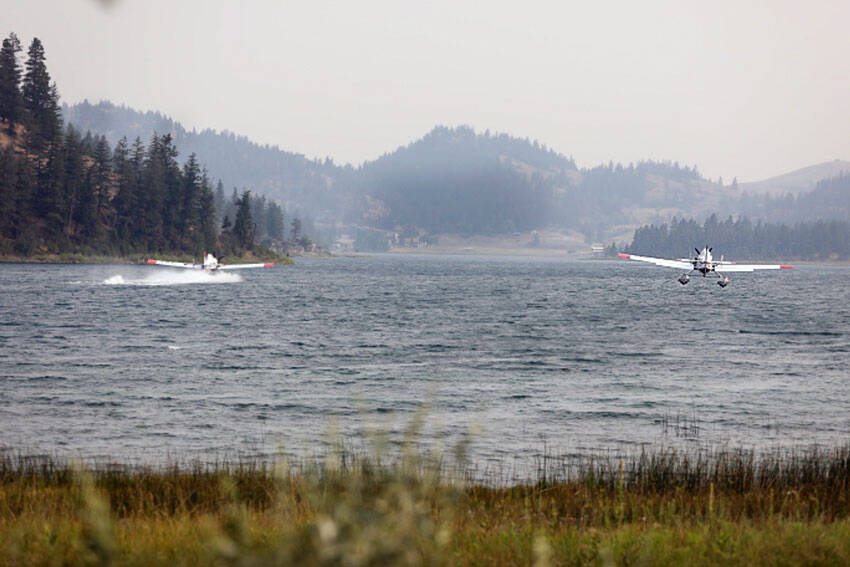 Two water-bomber planes gather water from Wannacut Lake to fight flames at the Rainbow Lake Fire on Palmer Mountain and the Wannacut Fire. The Rainbow Lake Fire was listed at 150 acres on Tuesday afternoon and the Wannacut lake fire was listed at 64 acres. Smoke from these fires and larger fires in the Methow, Chelan and lower British Columbia areas has settled in the Okanogan Valley. <em>Laura Knowlton/staff photo </em>